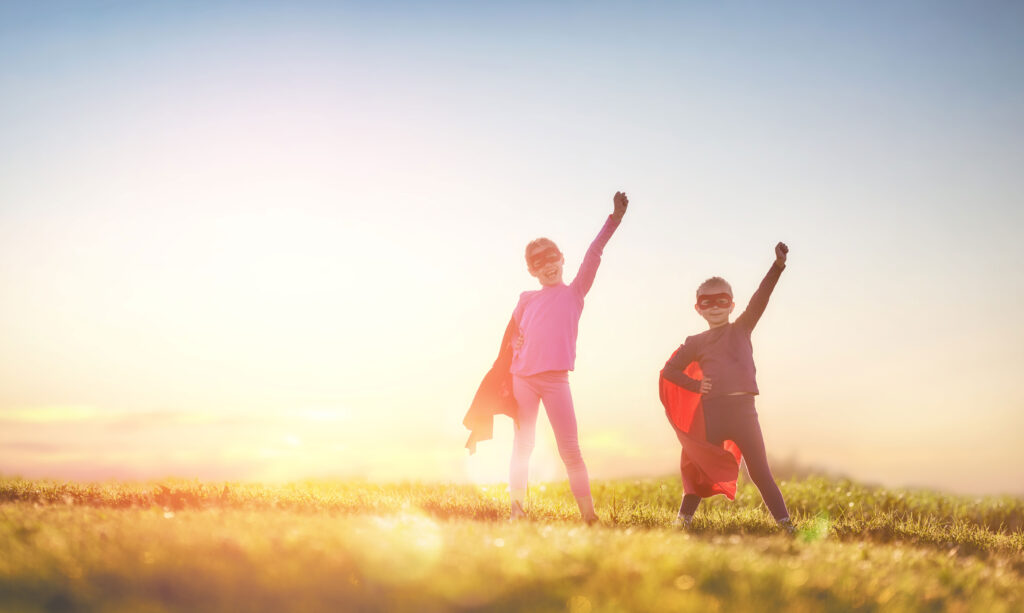 Zwei Kinder stehen in einem Heldenkostüm vor der Sonne